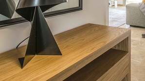 Un interior modern amb un moble de suport de fusta, una làmpada negra i vista a un passadís que condueix a una habitació amb rentadora.