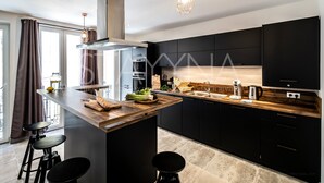 A modern kitchen with a central island, black cabinets, and a wooden countertop. - La Carioca (Nice)