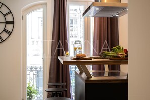 Een keuken met een houten aanrecht, een roestvrijstalen afzuigkap, een klok aan de muur en een stadszicht door grote ramen.