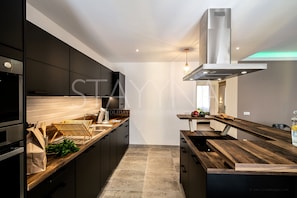 Una cocina moderna con armarios oscuros, encimera de madera y campana extractora de acero inoxidable.