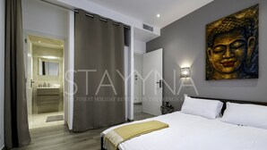 A modern hotel room with a large bed, a bathroom with a mirror, and a Buddha painting on the wall. - La Carioca (Nice)