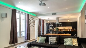 A modern living room with a black sofa, a glass coffee table, and a view of the kitchen in the background. - La Carioca (Nice)
