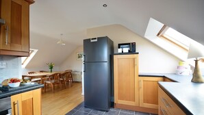 Une cuisine avec des meubles en bois, un réfrigérateur noir, un four à micro-ondes et un coin repas comprenant une table et des chaises.