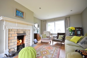 A living room with a fireplace, a green knitted pouf, a sofa with yellow pillows, and a bookshelf. - Ballydavid Sands 3 bedroom house VRBO (County Kerry)