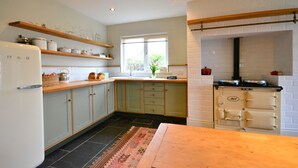 Cucina con mobili verde chiaro, un piano di lavoro in legno, forno integrato e una finestra vista verdeggiante.