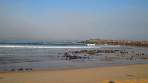 A beach with a rocky breakwater and calm waves.