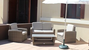 A patio with wicker furniture, including a sofa and chairs, and a white umbrella.