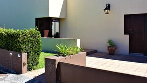 A modern building with a flat roof, a large window, and a door. There is a potted plant and a light fixture on the wall.