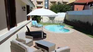 A patio with wicker furniture, a pool, and a white umbrella.