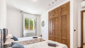 A bedroom with two beds, a wooden wardrobe, a window with a view of greenery, and a radiator.