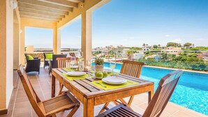 A wooden table set for dining with a view of a swimming pool and distant buildings.