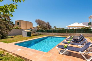 Una piscina rectangular con agua azul cristalina, rodeada por una terraza con baldosas. Se observan sillas de descanso con cojines y sombrillas, y un plato parabólico a la izquierda.