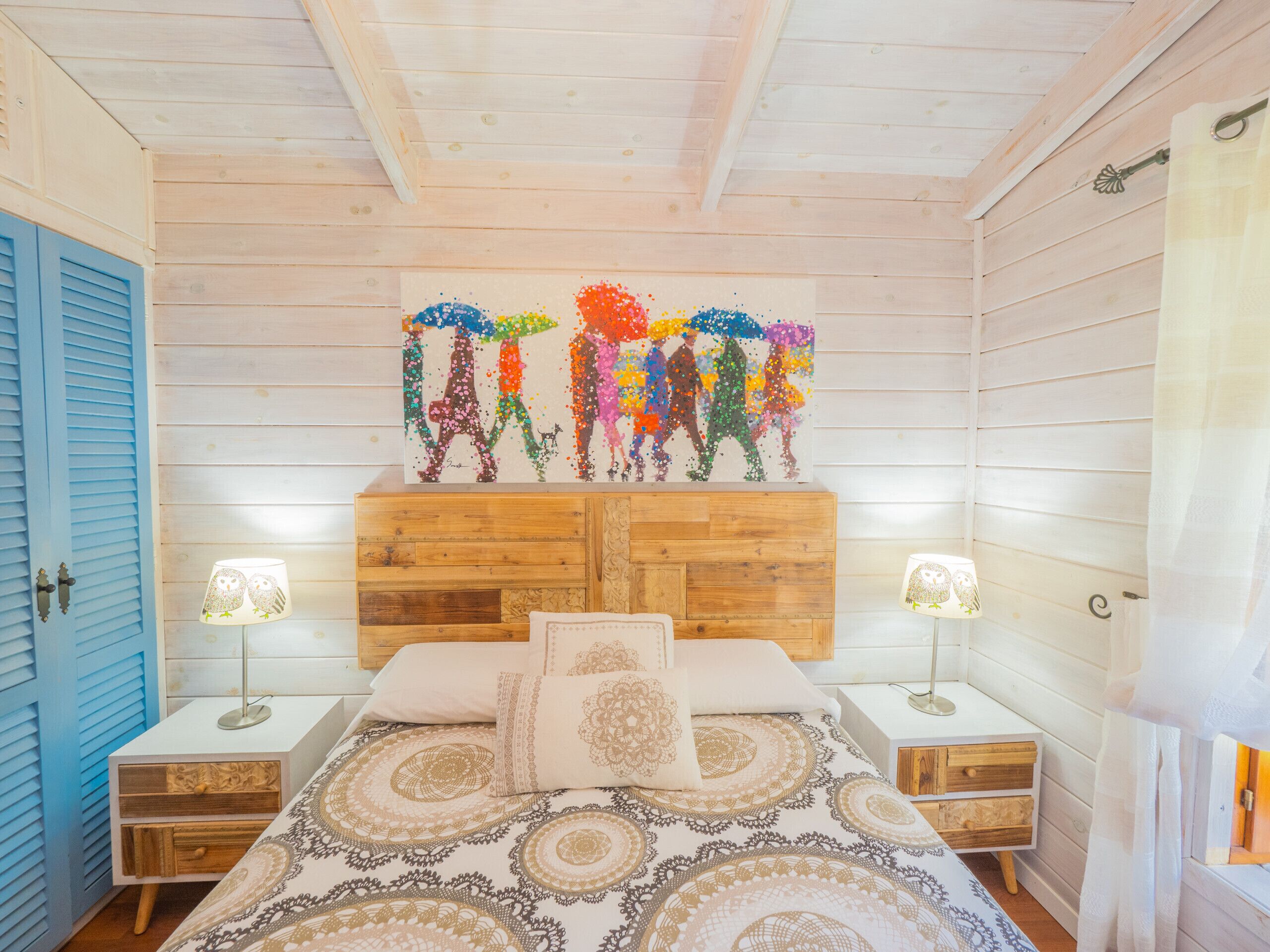 Ein Schlafzimmer einer Holzhütte mit einem Bett, zwei Nachttischen und einem farbenfrohen Kunstwerk an der Wand.
