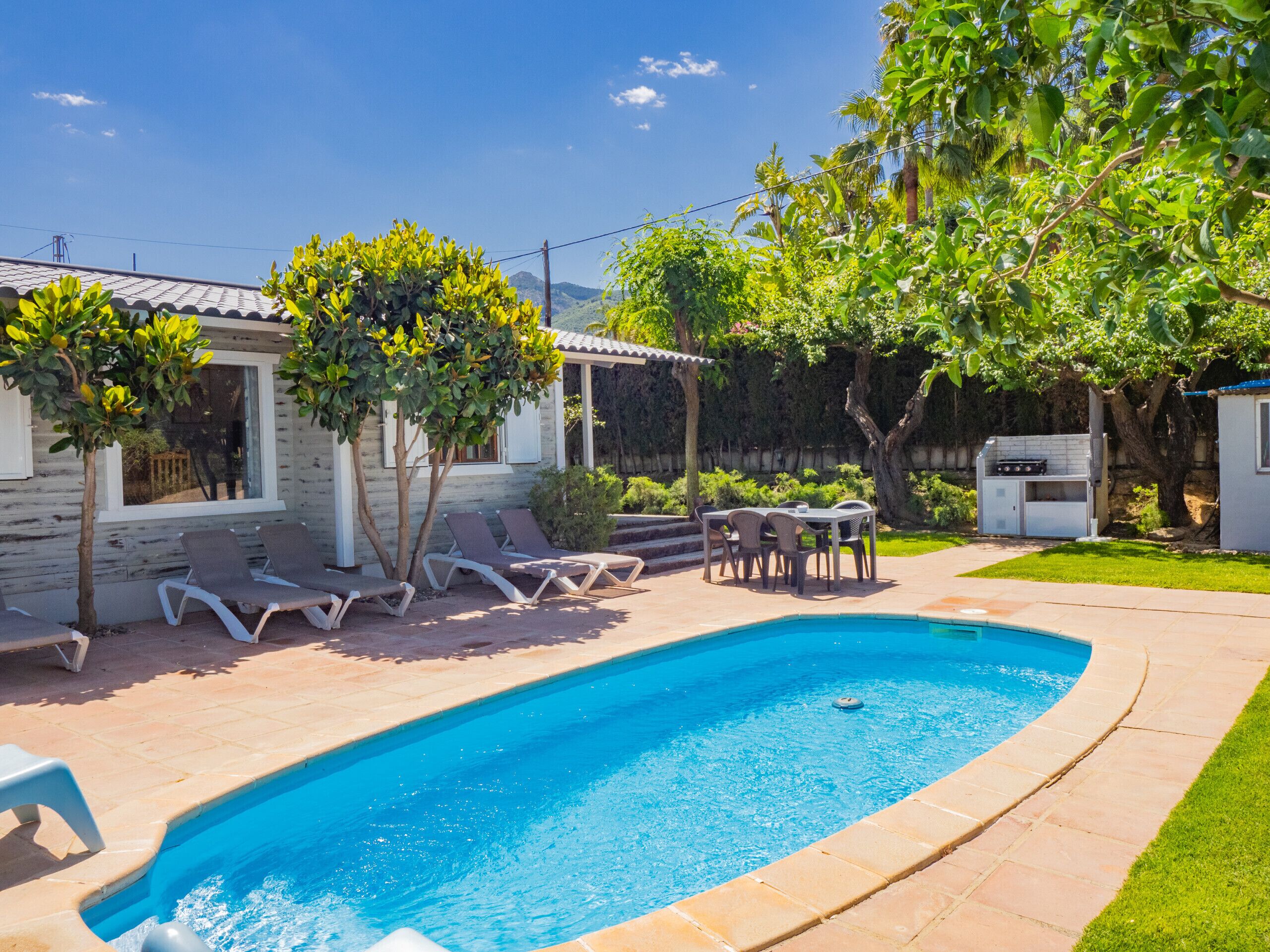 A swimming pool with lounge chairs and a barbecue area in a backyard.