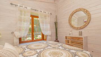 Een slaapkamer met een groot bed, een houten dressoir, een spiegel en een raam met gordijnen.