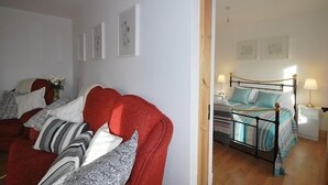 Un dormitorio con un sillón rojo, una cama con colcha a rayas y una mesita de noche con lámpara.