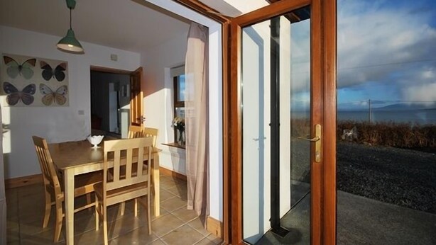 Un comedor con mesa y sillas de madera, una lámpara colgante verde y decoración de mariposas en la pared.