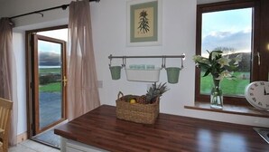 Una cocina con encimera de madera, una cesta de frutas, un reloj y una ventana con vistas al campo.