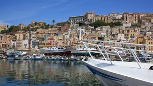 A marina with boats docked, surrounded by densely packed buildings with a mix of architectural styles. - Carabollace Estate - Mistral (Sciacca)