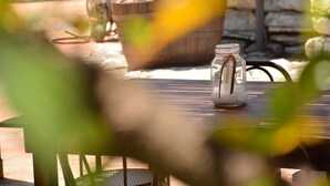 A glass jar with a straw on a wooden table, a potted plant, and a stone wall in the background. - Carabollace Estate - Mistral (Sciacca)