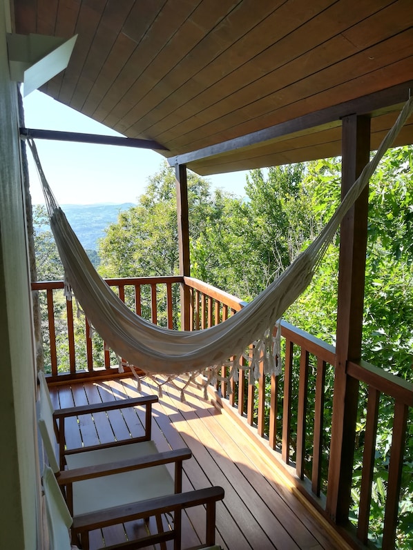 A hammock on a wooden deck with benches, overlooking a forested area.