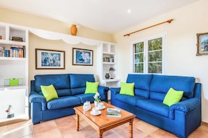 A living room with two blue sofas, a wooden coffee table, and a bookshelf with books and framed pictures.