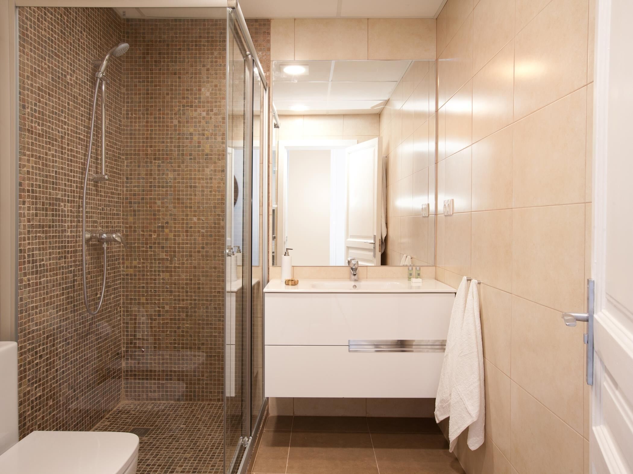 Un baño moderno con ducha envuelta en vidrio, un lavabo blanco y un espejo sobre el mueble.