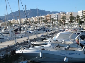 Un port de plaisance où sont amarrés de nombreux bateaux, un ciel dégagé et des bâtiments en arrière-plan.