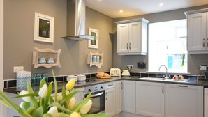 A modern kitchen with white cabinets, a stainless steel range hood, and a window providing natural light. - Morning Side 4 bedroom house VRBO (Dingle Peninsula)