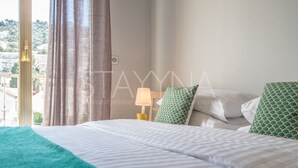 A hotel room with a bed, a nightstand, a lamp, and a view of the outside. - Coco 2 bedroom apartment VRBO (Nice)