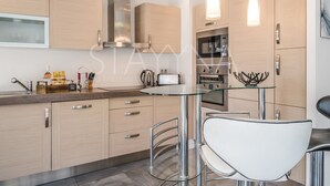 A modern kitchen with wooden cabinets, stainless steel appliances, and a glass dining table with bar stools. - Coco 2 bedroom apartment VRBO (Nice)