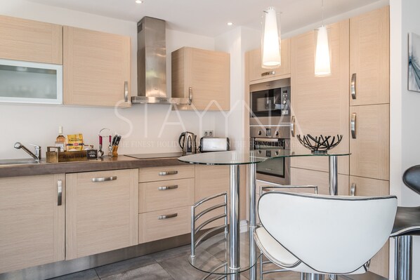A modern kitchen with wooden cabinets, stainless steel appliances, and a glass dining table with bar stools. - Coco 2 bedroom apartment VRBO (Nice)