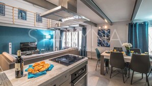 Una cucina moderna con isola centrale, zona pranzo con tavolo e sedie, e un'ampia finestra con tende.