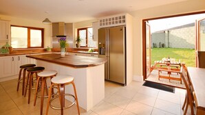 A modern kitchen with a central island, bar stools, a stainless steel refrigerator, and a view of the backyard. - Ceann Scribe 5 bedroom house VRBO (Dingle Peninsula)