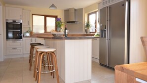 A kitchen with white cabinets, a stainless steel refrigerator, a built-in oven, and a bar stool area. - Ceann Scribe 5 bedroom house VRBO (Dingle Peninsula)