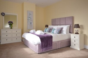 Een slaapkamer met een bed, nachtkastjes, een dressoir, een spiegel en een wanddecoratie.