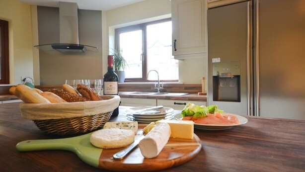 A kitchen with a wooden countertop, a wicker basket of bread, a bottle of wine, cheese, and a plate of food. - Ceann Scribe 5 bedroom house VRBO (Dingle Peninsula)