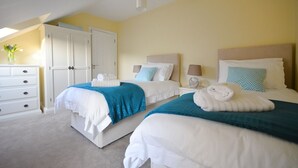 A hotel room with two beds, white bedding, teal throw blankets, and a white dresser. - Ceann Scribe 5 bedroom house VRBO (Dingle Peninsula)