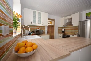 Una cocina moderna con armarios blancos, encimera de madera y un bol con naranjas.