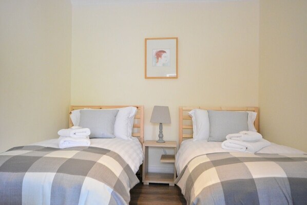 Una habitación de hotel con dos camas, cada una con una colcha a cuadros, una mesita de noche con una lámpara y un cuadro en la pared.