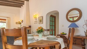 A dining area with a wooden table set for four, surrounded by chairs. There is a vase with flowers on the table, and a lamp on the right side. - CASA MIRANDA - Chalet with terrace in Valldemosa. Free WiFi (Valldemossa)