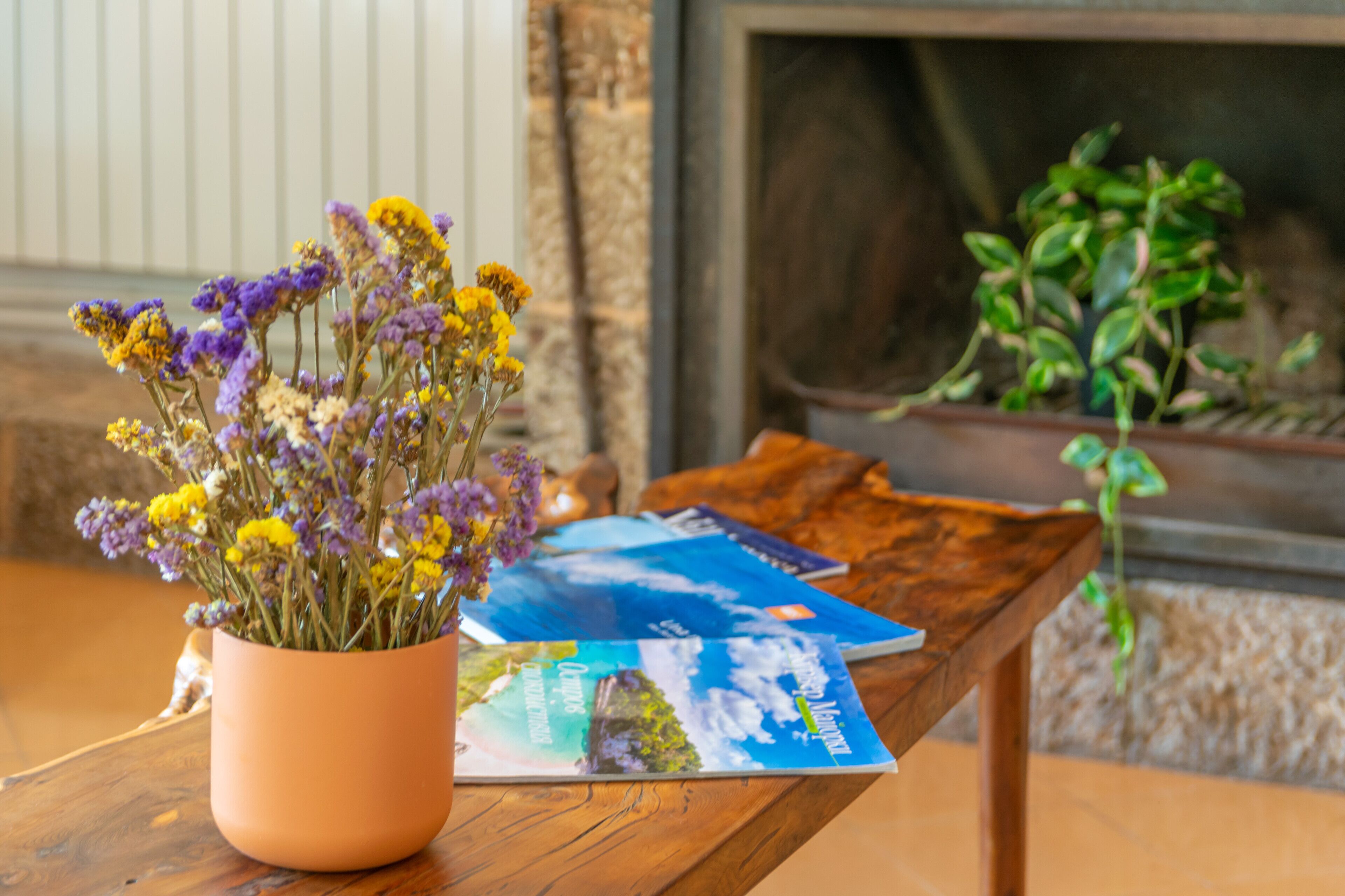 A wooden table with a vase of flowers and a few magazines.