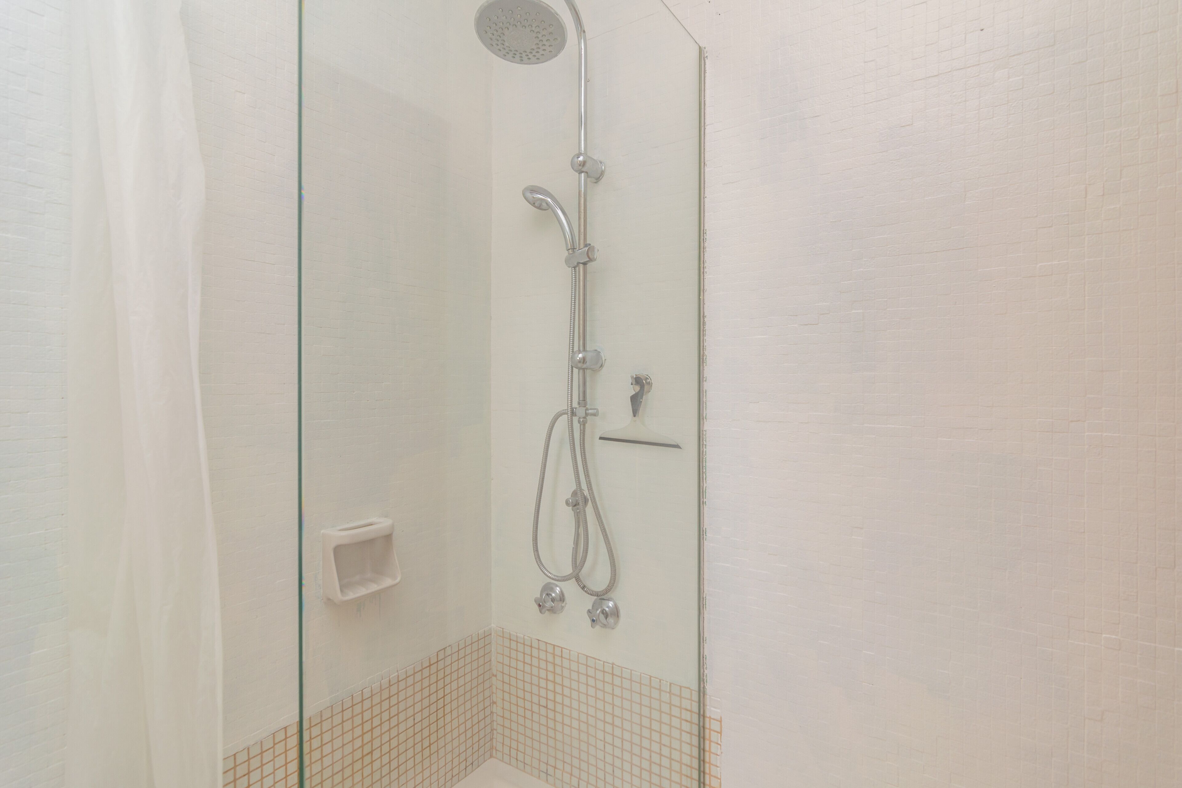 Eine gläserne Dusche mit Handbrause, Wandarmatur und einer kleinen Ablagefläche.