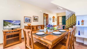 A dining area with a wooden table set for four, surrounded by chairs. A television is mounted on a wooden stand to the left. - Villa Marcolis Mar - Four Bedroom Villa, Sleeps 6 (Serpentona)