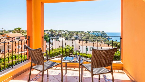 A balcony with wicker chairs and a table, overlooking a coastal town and the sea. - Villa Marcolis Mar - Four Bedroom Villa, Sleeps 6 (Serpentona)
