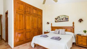 A bedroom with a large wooden wardrobe, a bed with a white bedspread, two bedside tables with lamps, and a wall-mounted painting. - Villa Marcolis Mar - Four Bedroom Villa, Sleeps 6 (Serpentona)