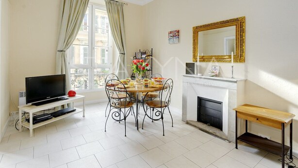 A living room with a TV, dining table, chairs, a fireplace, and a large mirror. - Lauren 2 bedroom apartment VRBO (Nice)