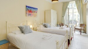 A bedroom with two beds, a wardrobe, a chair, and a balcony with curtains. - Lauren 2 bedroom apartment VRBO (Nice)