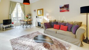 A living room with a sofa, a TV, a dining table, and a fireplace. - Lauren 2 bedroom apartment VRBO (Nice)