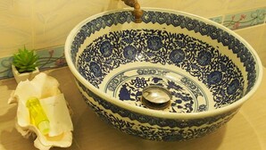Un lavamanos de baño con un lavabo azul y blanco decorativo, un grifo y una pequeña planta en maceta.